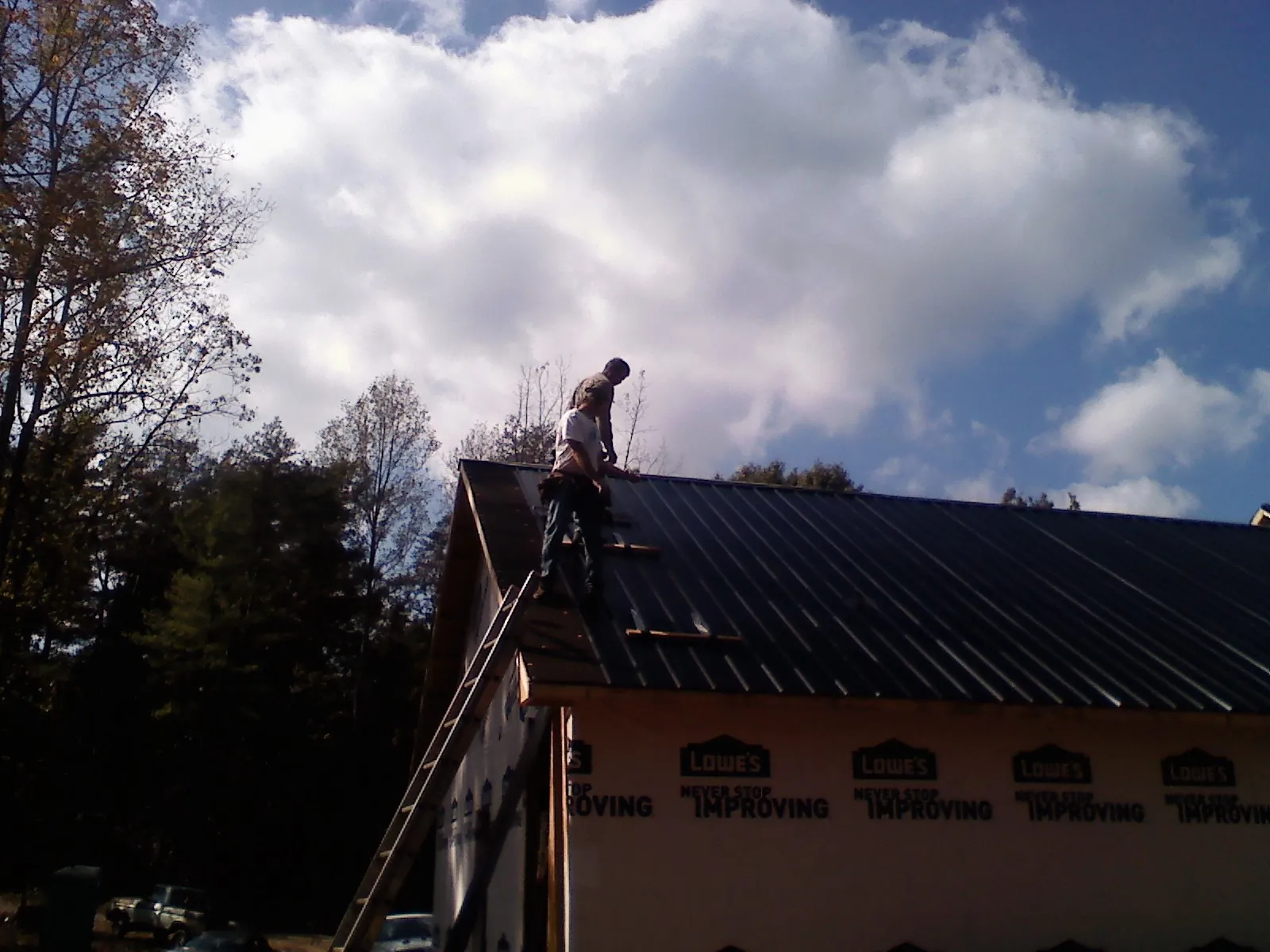 Roofer fastening dark metal panels high against a cloudy sky, from a Roof Inspection job in Drake